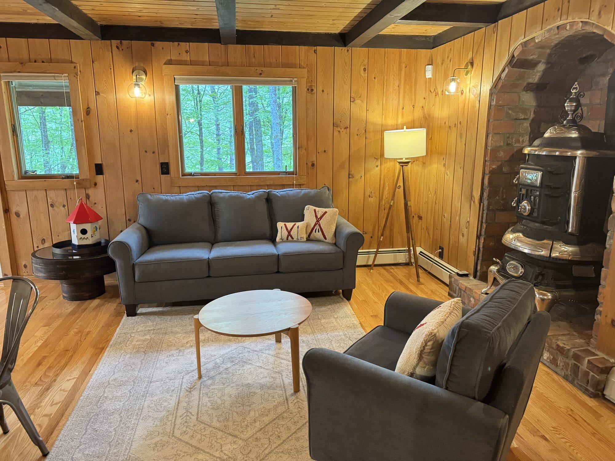 Pine-paneled living room with seating and a wood stove after a VelocityMaid Vermont reset