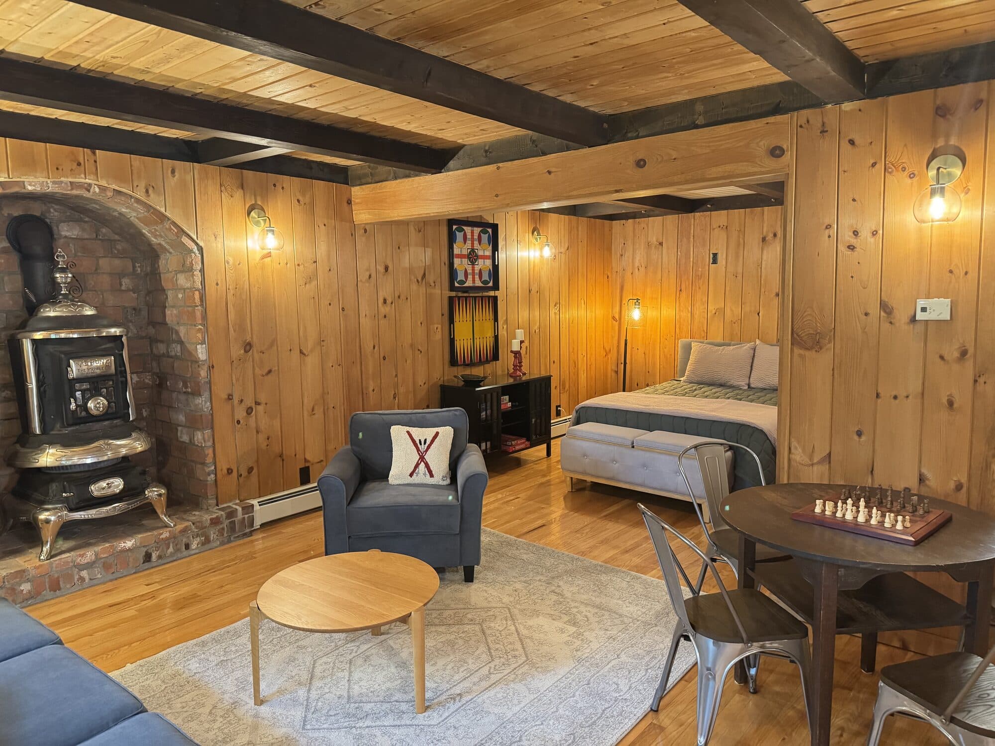Studio guest suite with made bed, sitting area, and wood stove after a Vermont turnover